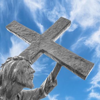 Statue of Jesus carrying his cross, on the way to his crucifixion. Ideal for the easter concept, resurrection and other. Blue sky with white clouds on background.