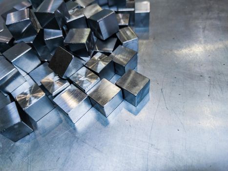 pile of small machined shiny steel cubes on metal surface, closeup with selective focus