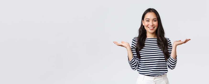 Lifestyle, people emotions and casual concept. Cute smiling asian woman introduce two products, hold hands sideways as if demonstrating products on palms, standing white background.