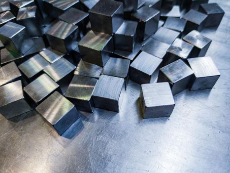 pile of small machined shiny steel cubes on metal surface, closeup with selective focus