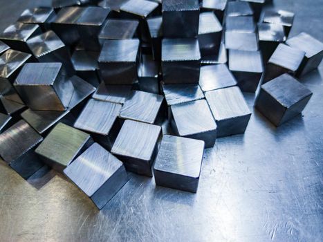 pile of small machined shiny steel cubes on metal surface, closeup with selective focus