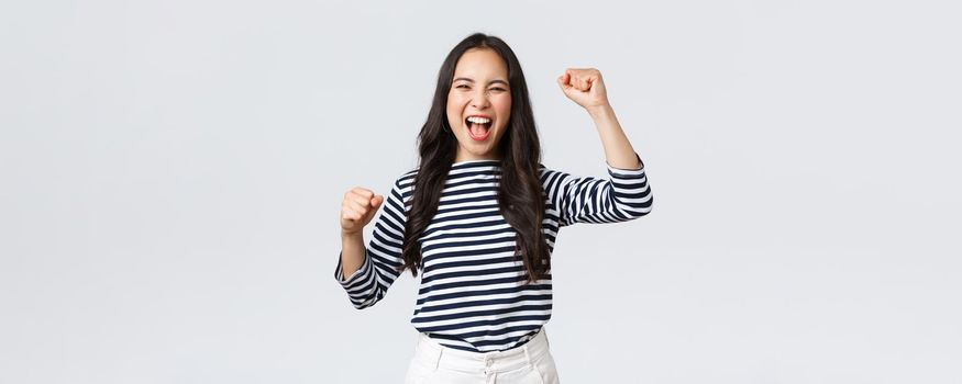 Lifestyle, people emotions and casual concept. Excited happy asian woman attend sport competition, rooting and chanting for team, raising hands up and shout yes supportive.