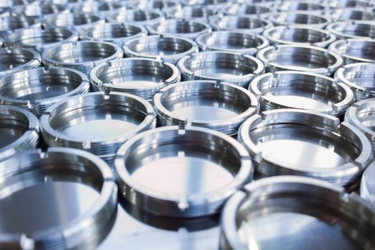 Shiny metal threaded rings after turning and milling. Silver colored rings on flat steel surface close-up full frame manufacturing background. Abstract small industrial parts batch processing concept,
