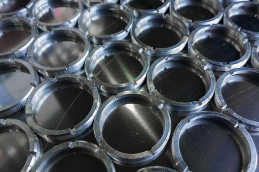 Shiny metal threaded rings after turning and milling. Silver colored rings on flat steel surface close-up full frame manufacturing background. Abstract small industrial parts batch processing concept,