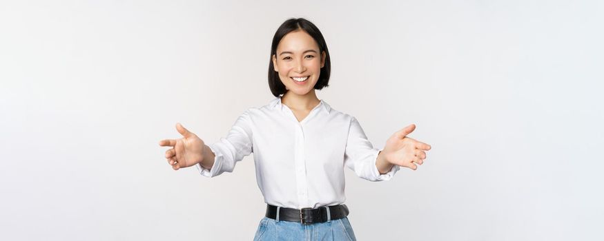 Image of smiling asian woman welcoming guests clients, businesswoman stretching out open hands, greeting, standing over white background.