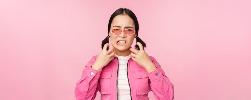 Image of angry, pissed off korean adult female model, shaking fists and shouting, screaming outraged, standing over pink background.