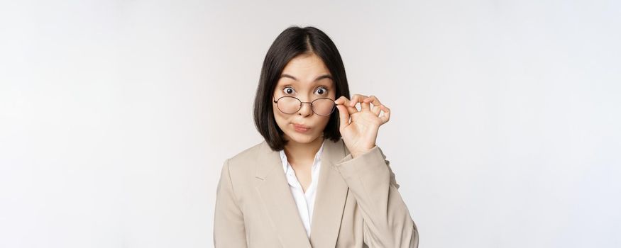 Portrait of businesswoman take-off glasses and looking surprised at camera, standing over white background.