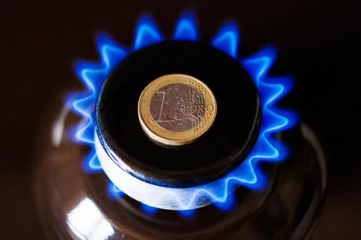 gas stove burner with one euro coin laid on top, burning natural gas with blue flame, gas price in European Union concept