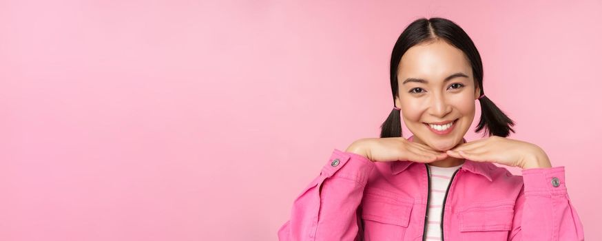 Skin care and cosmetology concept. Beautiful asian girl smiling and laughing, showing clean healthy facial skin, posing against pink background. Copy space