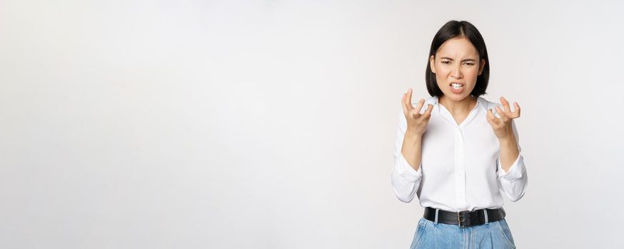 Image of angry pissed off woman shaking from anger, clench hands and grimacing furious, annoyed and outrated, standing over white background.