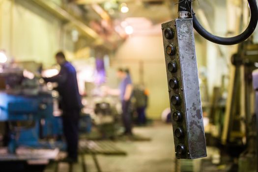 closeup view of shop crane control panel box with blurry milling workers in the background
