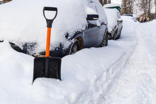 Plastic snow shovel in front of snow-covered parked cars row at winter morning.
