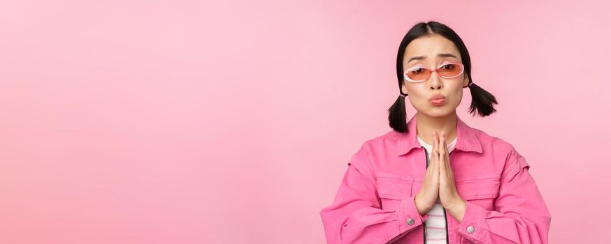 Please. Cute asian girl asking favour, begging, standing against studio background. Copy space