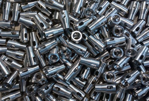 A lot of small equal shiny steel parts flat background. Raw metal surface after cnc turning and milling reflects light like silver.