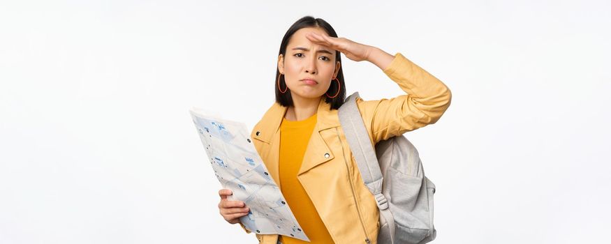 Image of young asian girl tourist, traveller with map and backpack posing against white studio background. Copy space