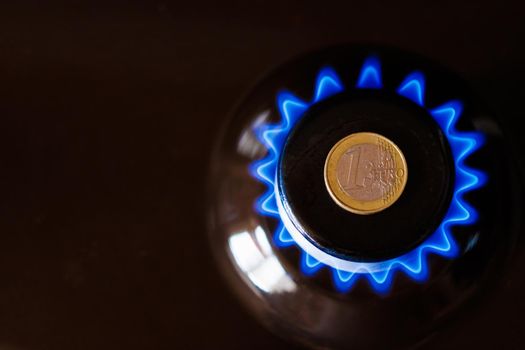 gas stove burner with one euro coin laid on top, burning natural gas with blue flame, gas price in European Union concept