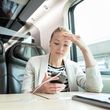 Businesswoman communicating on cellphone using headphone set while traveling by train in business class seat.