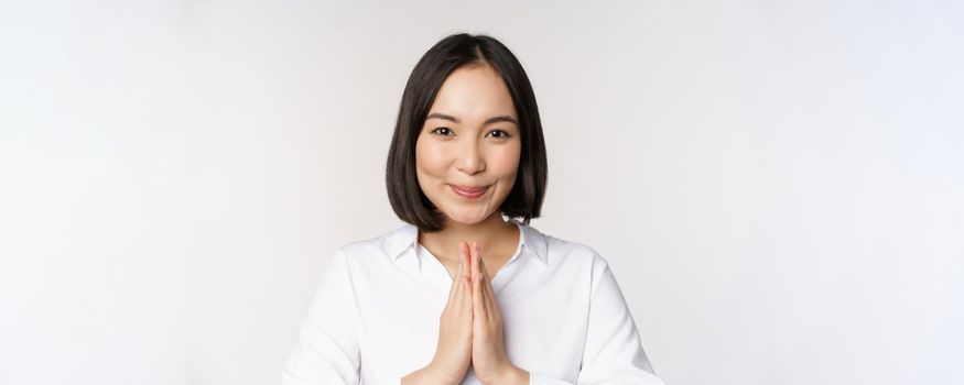 Close up portrait of young japanese woman showing namaste, thank you arigatou gesture, standing over white background.