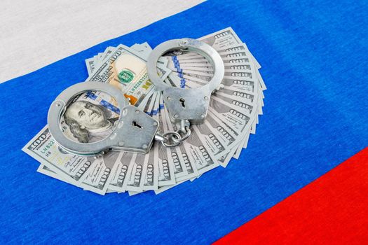 silver metal police handcuffs over paper dollar banknotes of United States of America over national flag of Russian Federation, concept of foreign currency prohibition