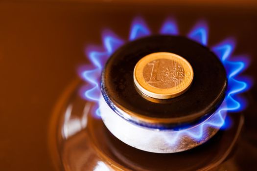 gas stove burner with one euro coin laid on top, burning natural gas with blue flame, gas price in European Union concept