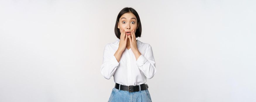 Portrait of surprised young office woman, asian businesswoman gasping amazed, saying wow, standing impressed of news against white background.