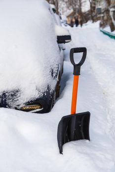 Plastic snow shovel in front of snow-covered parked cars row at winter morning.