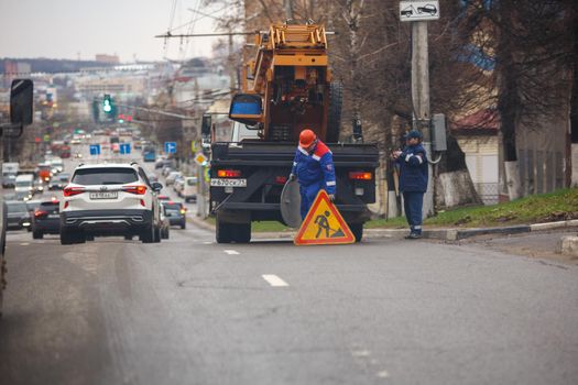 maintenance worker placing road work sign behind truck with cradle on summer day street of Tula, Russia - April 19, 2021