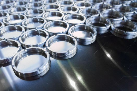 Shiny metal threaded rings after turning and milling. Silver colored rings on flat steel surface close-up full frame manufacturing background. Abstract small industrial parts batch processing concept,