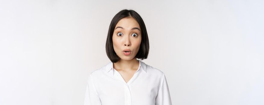 Close up portrait of young asian female model looking amazed at camera, smiling white teeth, standing against white background.