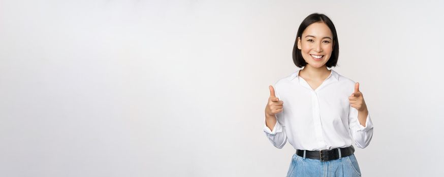 Its you congrats. Smiling attractive asian woman, businesswoman pointing fingers at camera with pleased face, complimenting, inviting you, standing over white background.