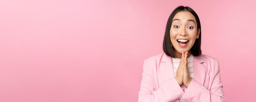 Portrait of happy asian office lady, ceo businesswoman in suit rejoicing and laughing, winning, celebrating, achieve goal and rejoice, standing over pink background.