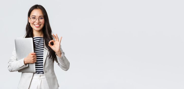 Business, finance and employment, female successful entrepreneurs concept. Young confident businesswoman in glasses, showing okay gesture, hold laptop, guarantee best service quality.