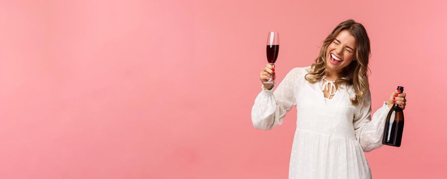 Holidays, spring and party concept. Portrait of excited and emotive good-looking blond girl dancing and celebrating, having fun saying yeah singing closed eyes, hold glass wine and bottle.