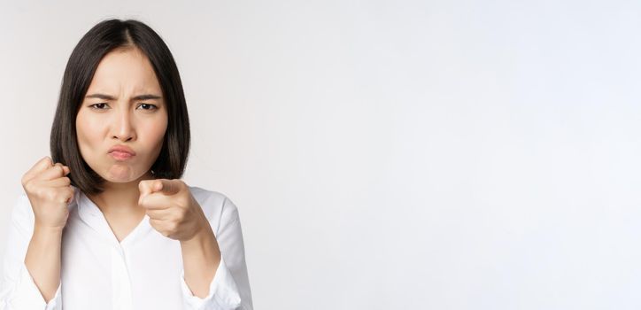 Close up of angry young woman clench fists, ready for fight, fighting, standing over white background.