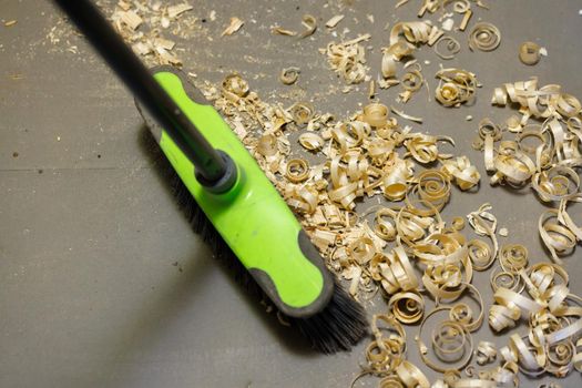 a small pile of wood shavings on a gray linoleum floor with plastic broom brush