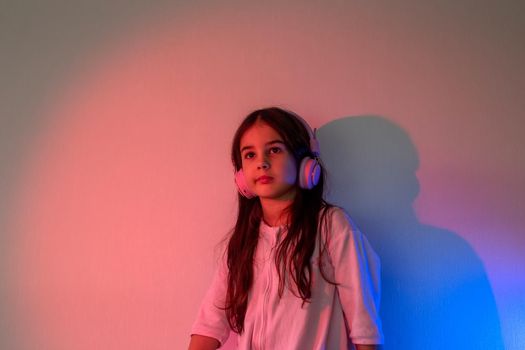 Beautiful girl in pink headphones, with loose dark hair, listening to music in neon pink blue light