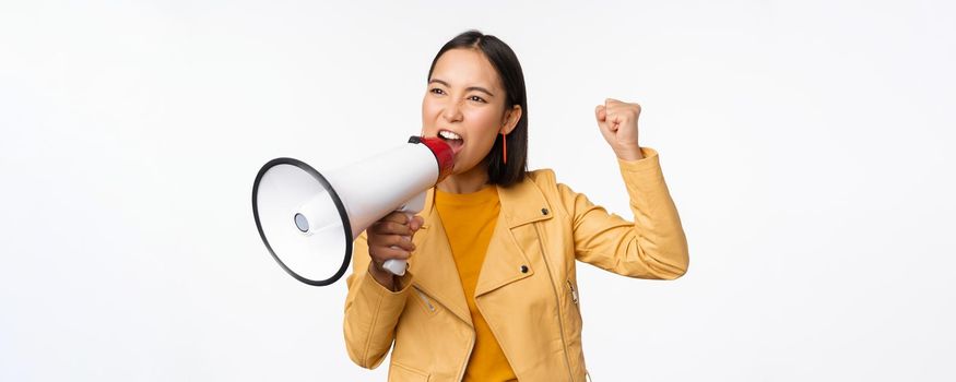 Portrait of young asian woman protester, screaming in megaphone and protesting, standing confident against white background.