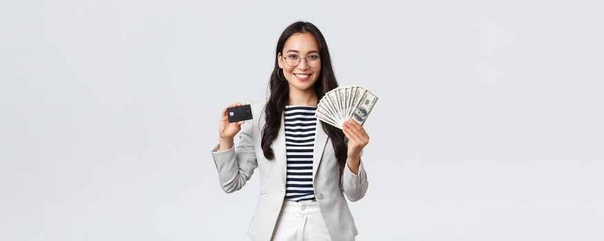 Business, finance and employment, entrepreneur and money concept. Successful asian businesswoman showing how increase income, hold credit card and money, smiling camera.