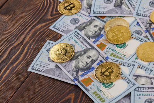 yellow bitcoin coins scattered over US dollar paper banknotes on wooden background, cryptocurrency and fiat money exchange concept