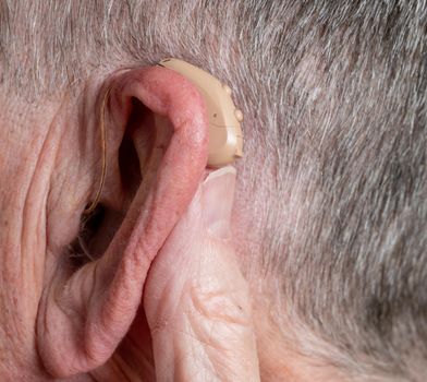 Macro close up of tiny modern hearing aid placed behind the ear of senior adult man