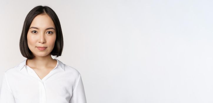 Close up portrait of korean young asian woman, professional, looking confident and assertive at camera, white background. Business people concept