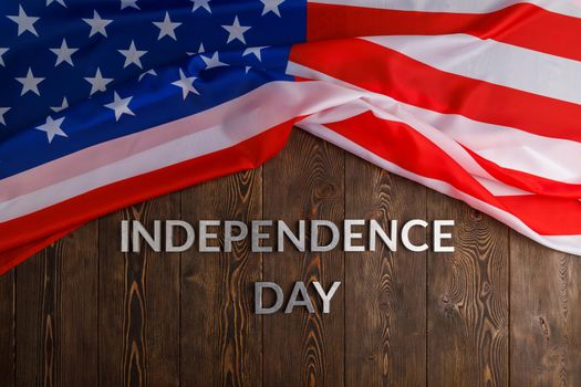 the words independence day laid with real metal letters on brown wooden planks surface with crumpled united states of america flag.