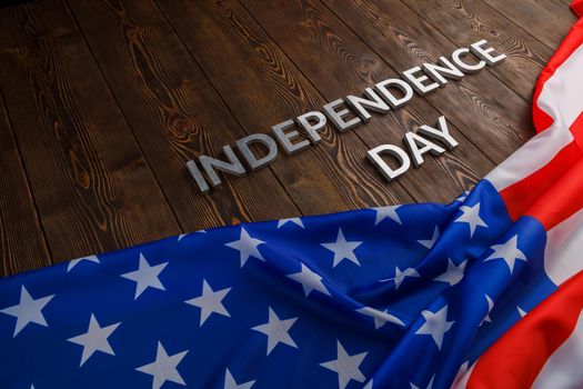 the words independence day laid with real metal letters on brown wooden planks surface with crumpled united states of america flag.