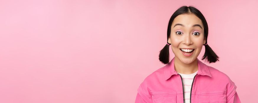 Close up portrait of beautiful asian girl looking enthusiastic and smiling, laughing and smiling, standing happy against pink background.