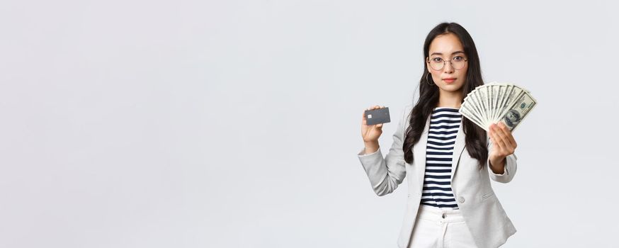 Business, finance and employment, entrepreneur and money concept. Successful asian businesswoman showing how increase income, hold credit card and money, smiling camera.