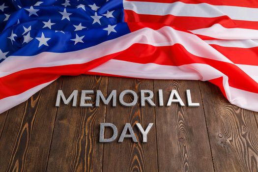 the words memorial day laid with silver metal letters on wooden board surface with crumpled usa flag above.