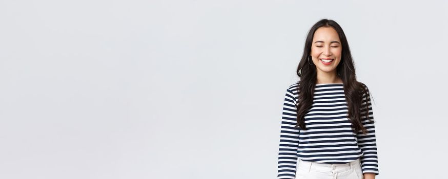 Lifestyle, people emotions and casual concept. Carefree, happy pretty asian woman in striped shirt close eyes and laughing sincere, having fun, funny moment, standing white background.