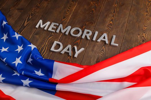 the words memorial day laid with silver metal letters on wooden board surface with crumpled usa flag.