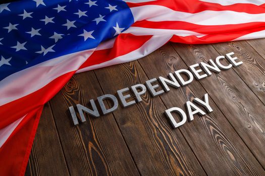 the words independence day laid with real metal letters on brown wooden planks surface with crumpled united states of america flag.