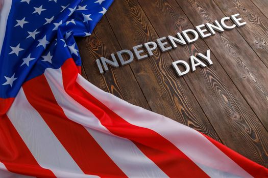 the words independence day laid with real metal letters on brown wooden planks surface with crumpled united states of america flag.